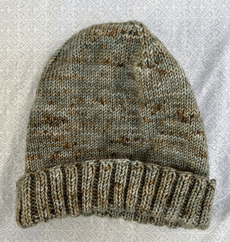 Multicolored (green, brown, gray, and blue) knit hat on neutral background